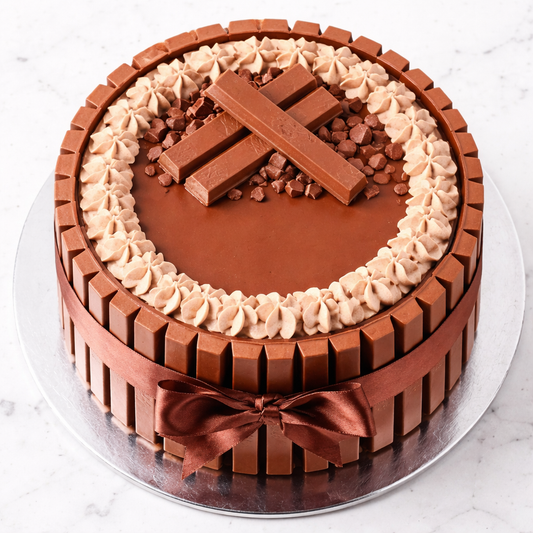 A tall Belgstrew KitKat Cake surrounded by chocolate wafer bars and topped with chocolate curls and whole KitKat pieces.