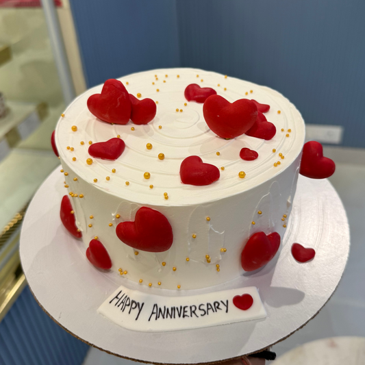 A bespoke Belgstrew Love Themed cake with red fondant hearts and elegant gold-leaf detailing on a smooth white base.