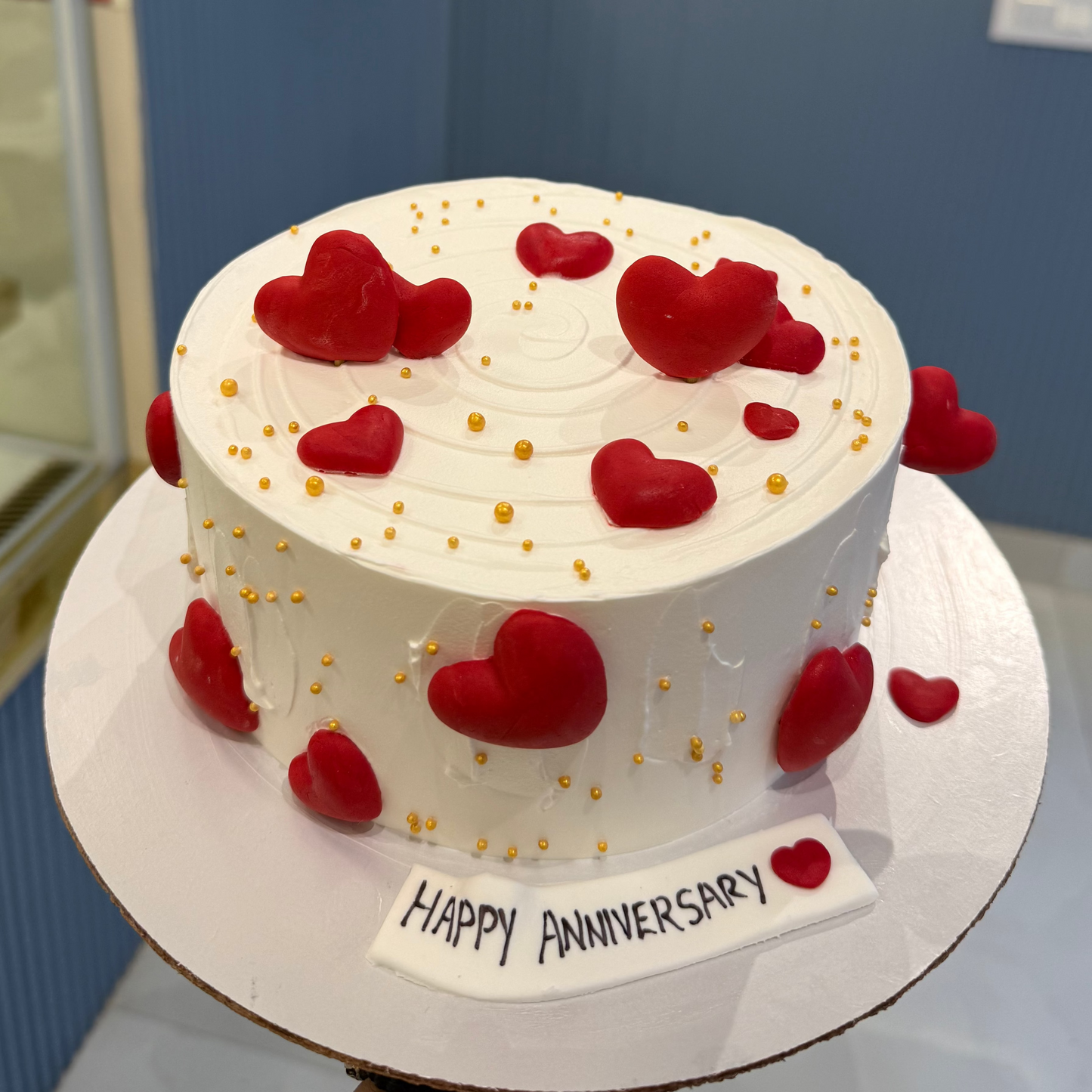 A bespoke Belgstrew Love Themed cake with red fondant hearts and elegant gold-leaf detailing on a smooth white base.