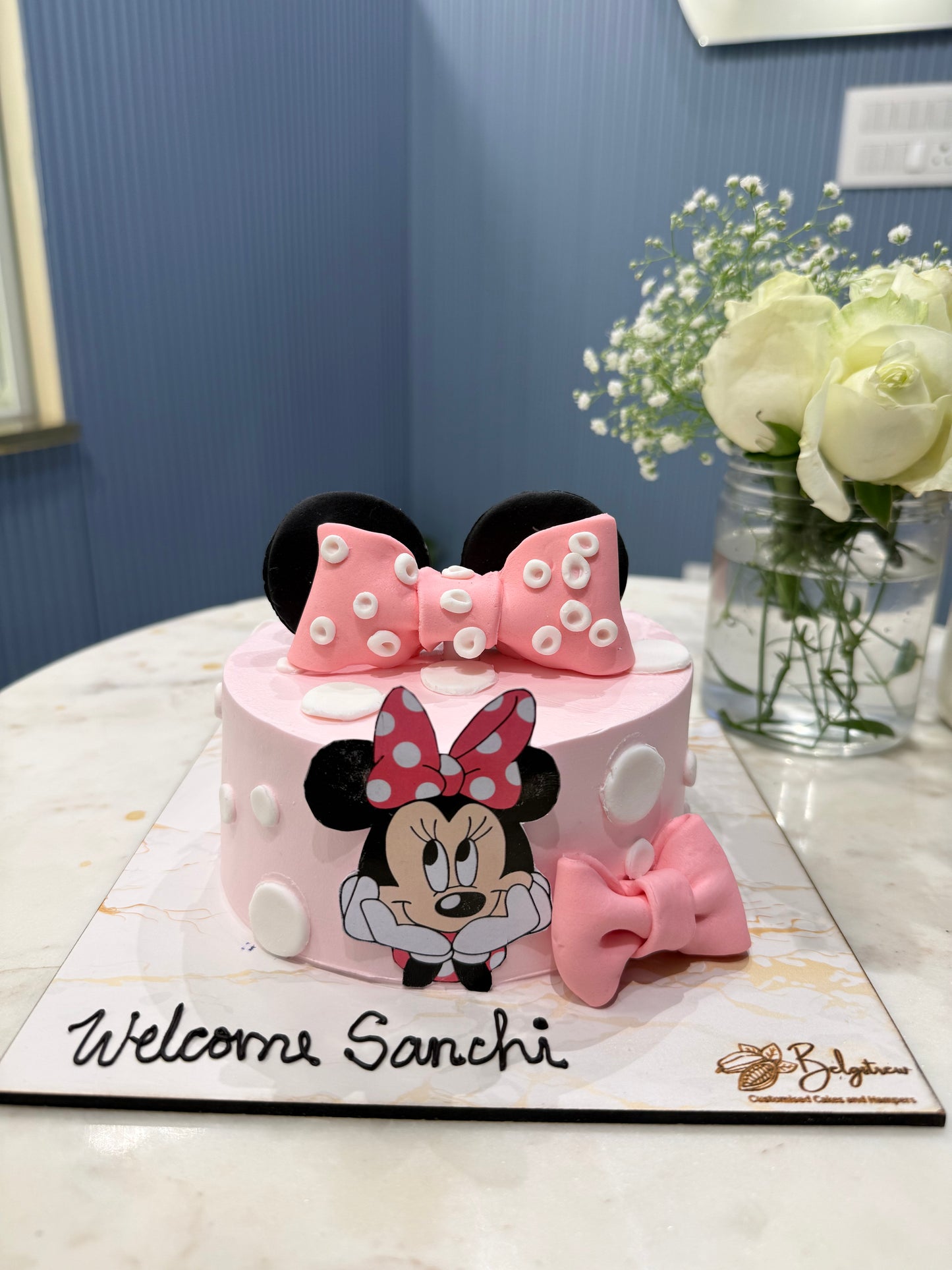 A bespoke Belgstrew Welcome Baby Girl cake featuring a large pink fondant Minnie Mouse bow and white polka dots on a tiered cake.