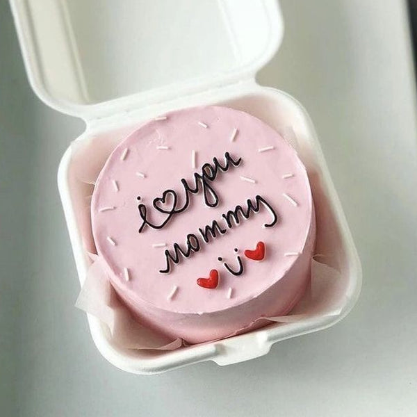 A pink minimalist bento cake in a sustainable white box with white sprinkles and red heart decorations, featuring "i โก you mommy" hand-piped in dark script. Part of the Belgstrew Mother's Day collection.