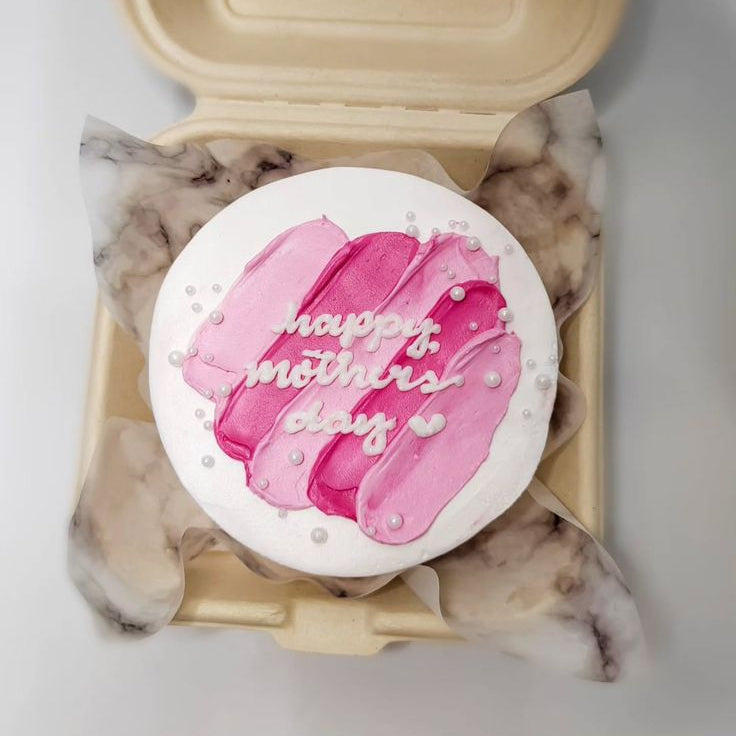 A white bento cake with abstract pink and magenta frosting strokes, white edible pearls, and "happy mother's day" written in white script.