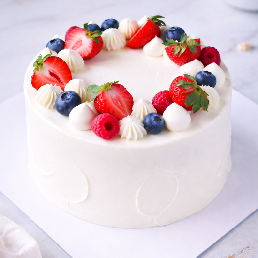Top view of a Belgstrew Fresh Fruit Cake decorated with colorful slices of kiwi, grapes, and seasonal berries.