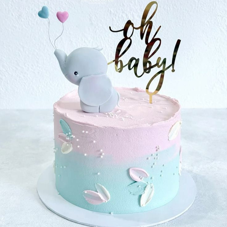 A textured pink and mint blue ombré baby shower cake decorated with palette knife details, topped with a grey fondant baby elephant holding tiny pink and blue heart balloons and a gold Oh Baby topper.