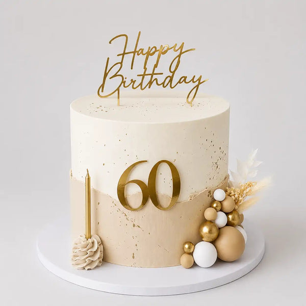 A tall round milestone birthday cake with a smooth white top half and a beige fault line bottom half decorated with gold splatters, a gold number 60, white and gold spheres, and dried boho florals as seen in image.