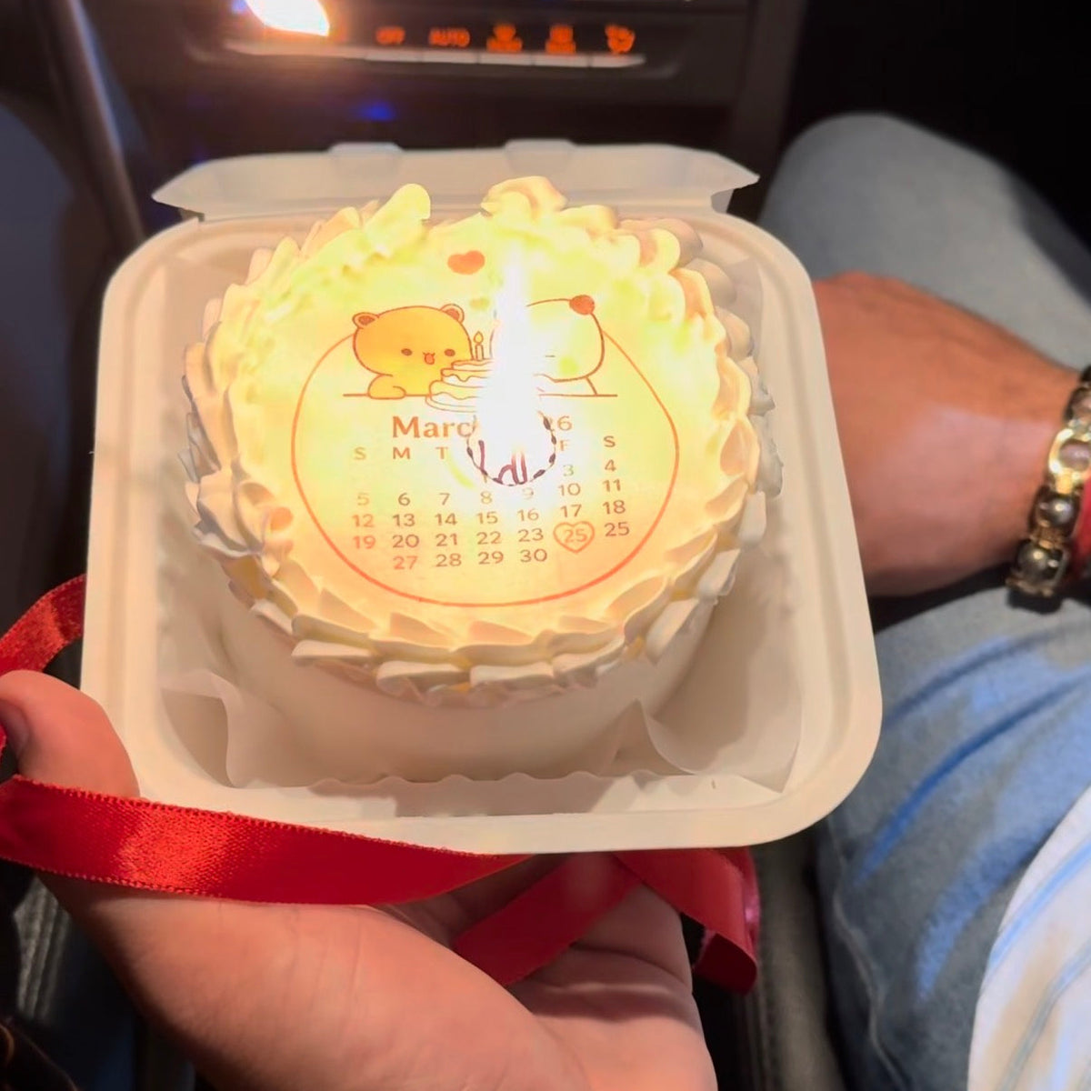 A 300g eggless bento cake where a printed calendar layer is being torched at the birth date to reveal a hidden "Happy Birthday" message underneath.