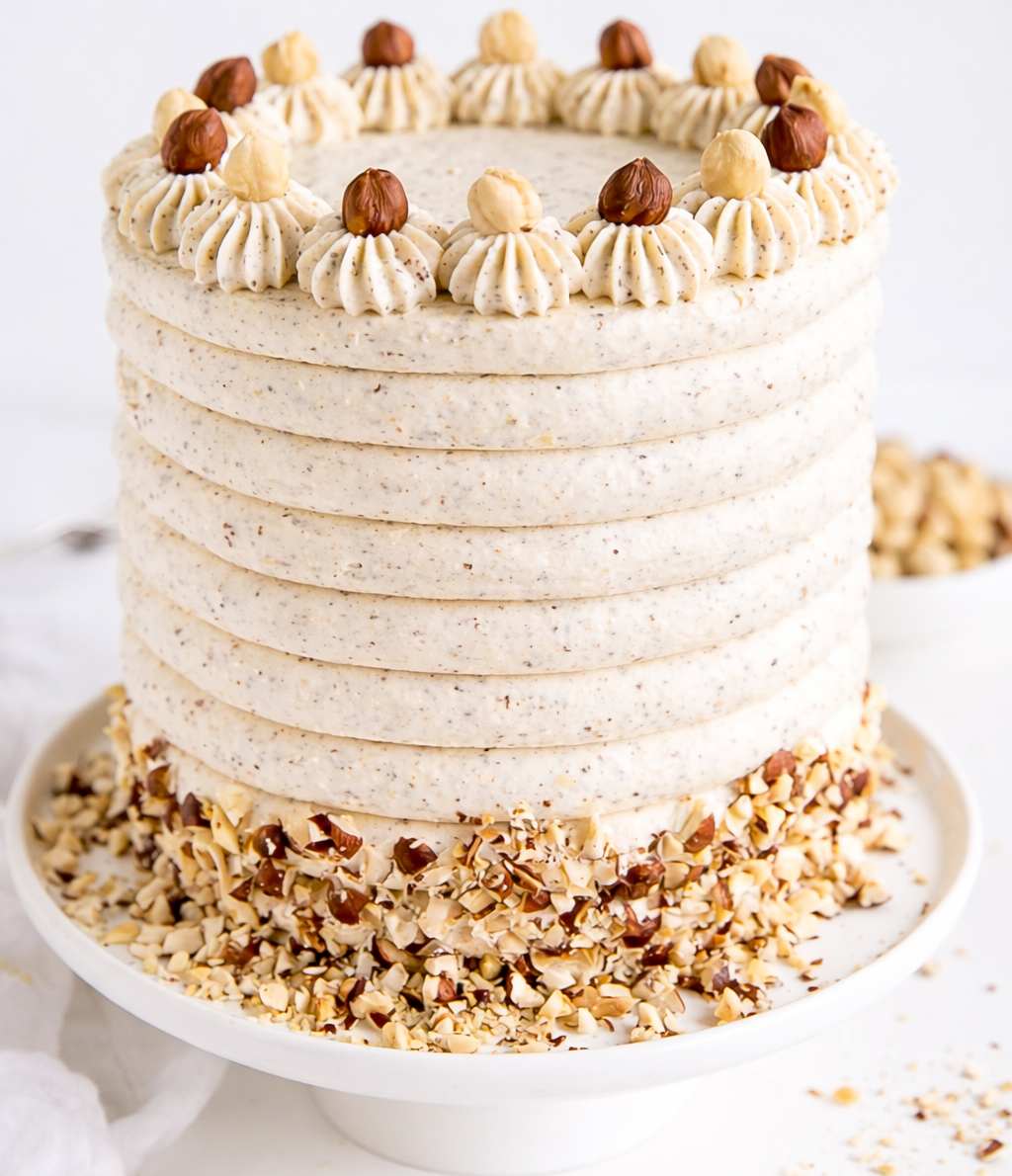 A white Belgstrew Vanilla Cake decorated with golden hazelnut praline bits and smooth cream swirls.