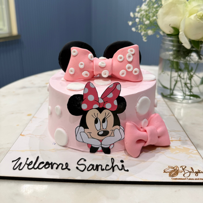 A bespoke Belgstrew Welcome Baby Girl cake featuring a large pink fondant Minnie Mouse bow and white polka dots on a tiered cake.