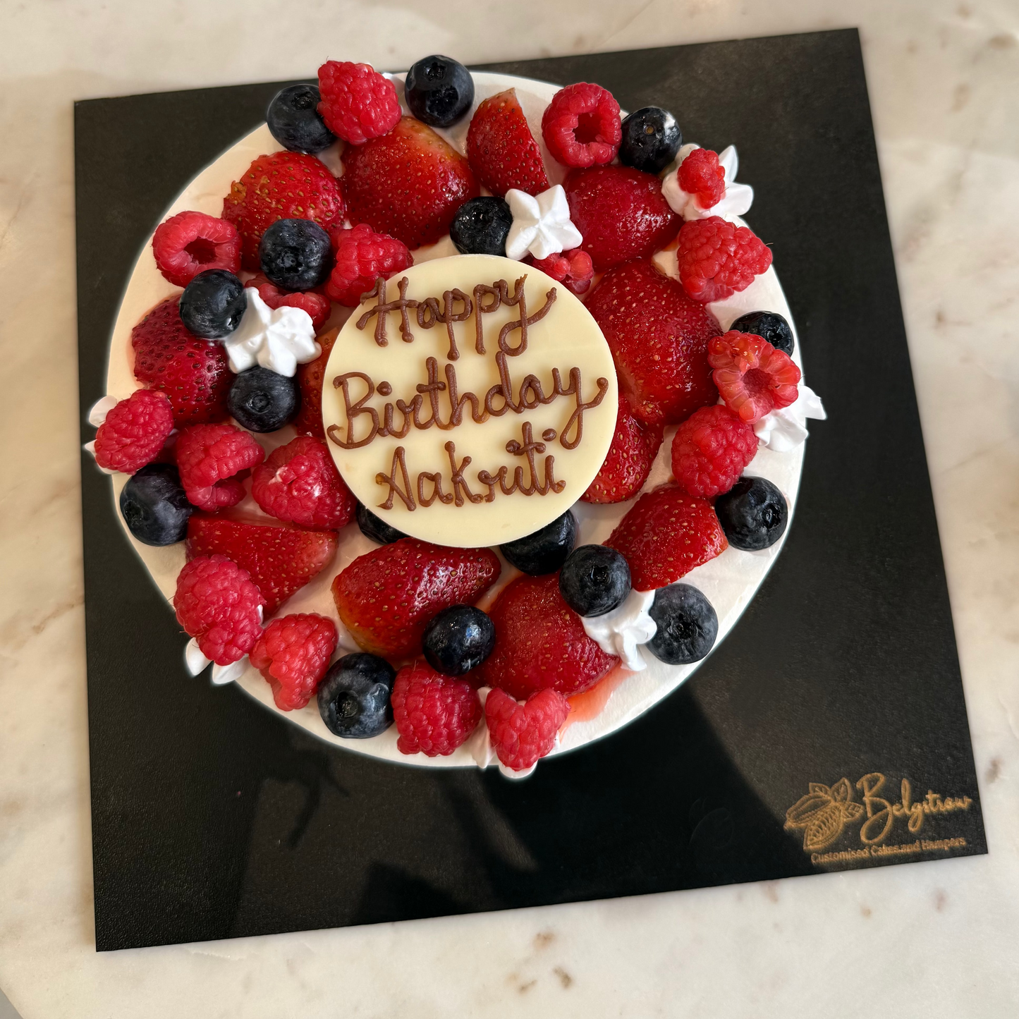 A decadent Belgstrew Chocolate Truffle Cake overflowing with fresh red strawberries, dark blueberries, and vibrant raspberries.