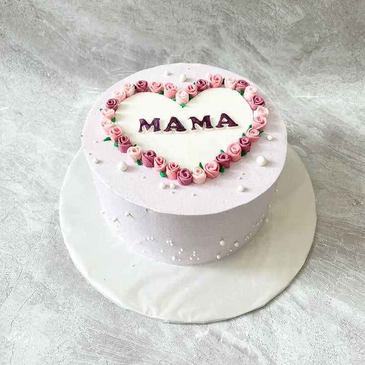 A lavender-colored cake with a white heart on top, bordered by pink and purple piped roses and "MAMA" written in the center.