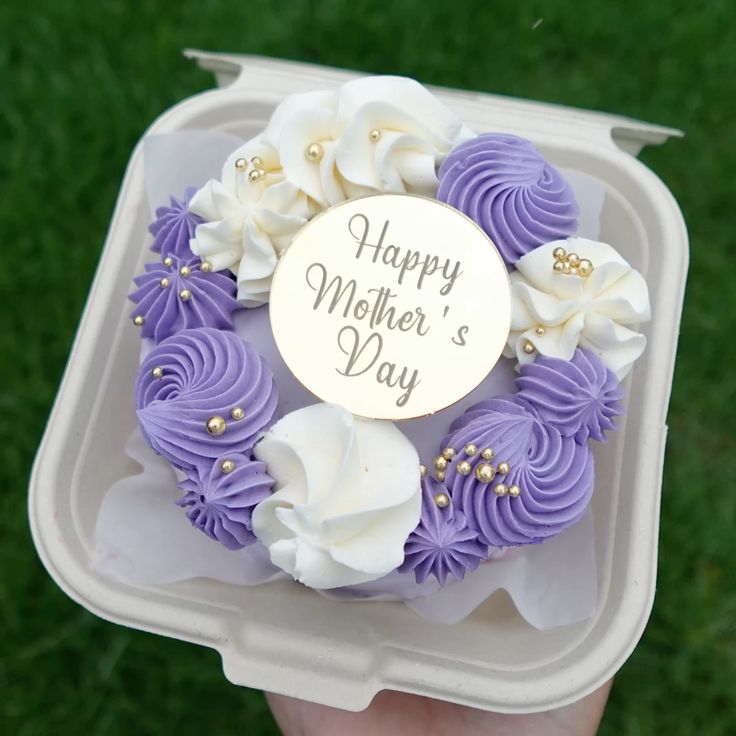 A purple and white rosette wreath bento cake with gold sprinkles and a gold Happy Mother's Day topper in a bento box.