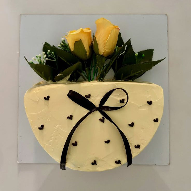 A vertical half-circle yellow cake designed to look like a flower bouquet, featuring fresh yellow roses, a black ribbon, and tiny black piped hearts.