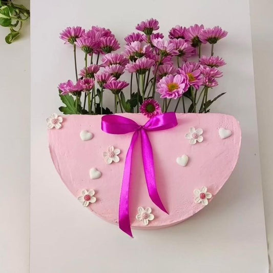 A vertical pink half-circle cake designed as a flower bag, overflowing with fresh purple chrysanthemums and decorated with a magenta ribbon.