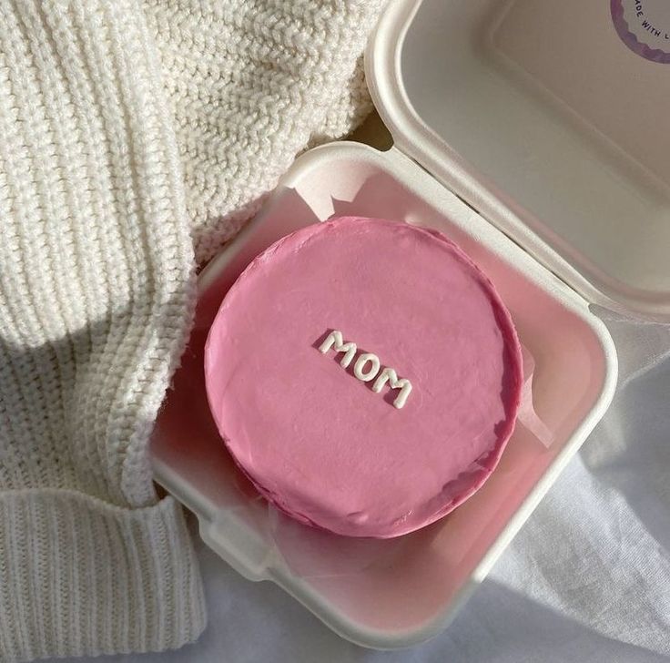 A vibrant pink textured bento cake in a white box with "mom" hand-piped in white lowercase letters.