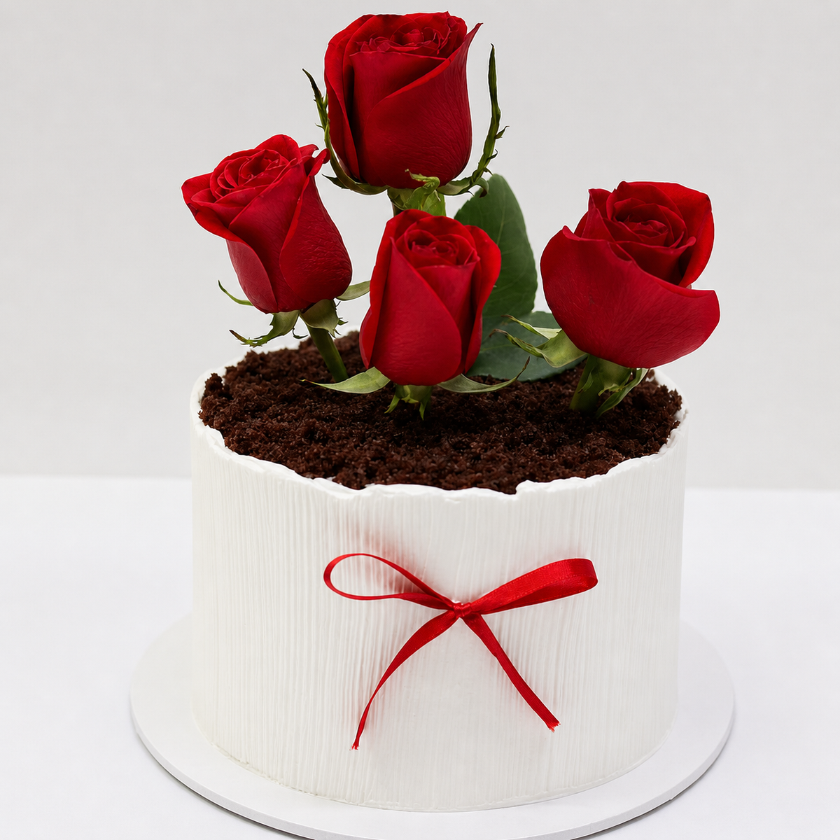 A white vertically textured cake shaped like a flower pot with dark chocolate soil, fresh red roses, and a small red ribbon.