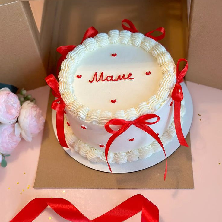 A white vintage piped Lambeth cake decorated with red silk ribbons and small red hearts.