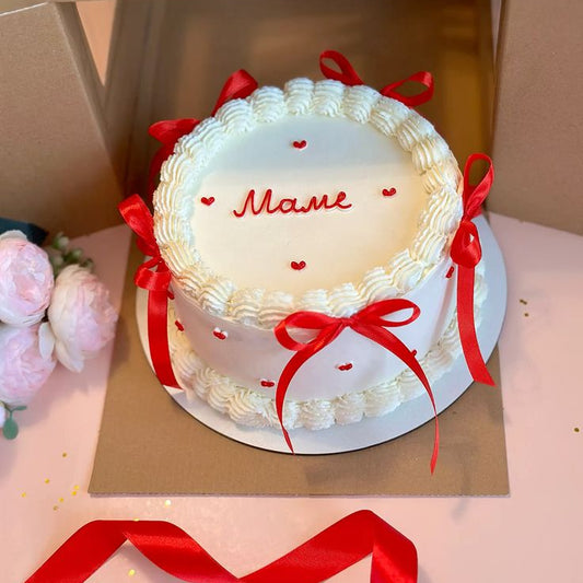 A white vintage piped Lambeth cake decorated with red silk ribbons and small red hearts.