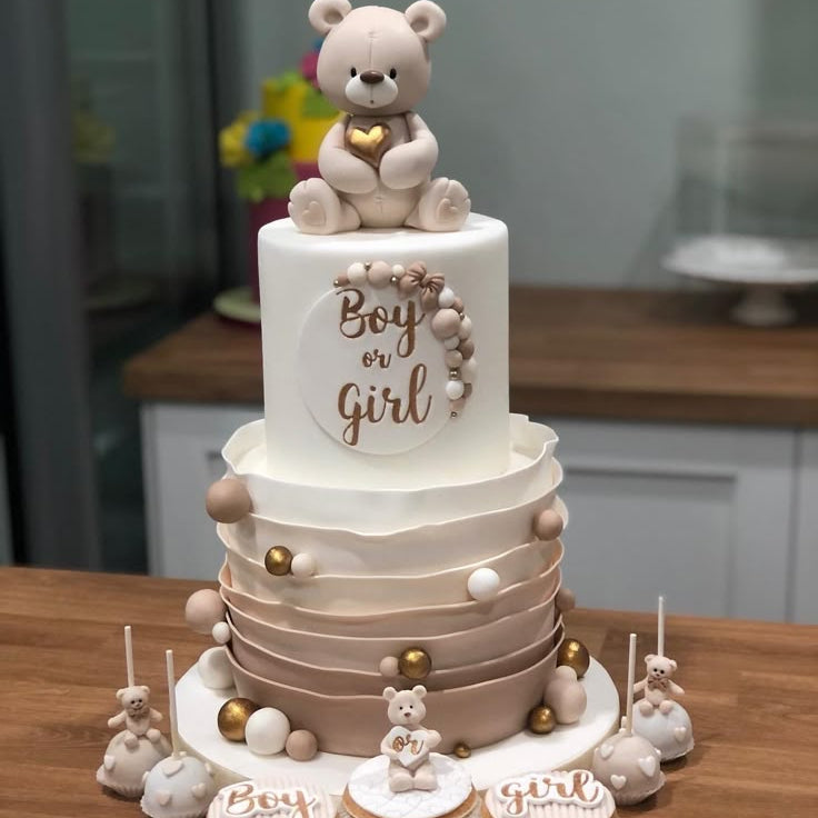 Two-tiered Baby Shower cake with teddy bear decorations and 'Boy or Girl' text on a wooden table.