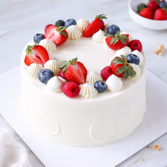 Top view of a Belgstrew Fresh Fruit Cake decorated with colorful slices of kiwi, grapes, and seasonal berries.