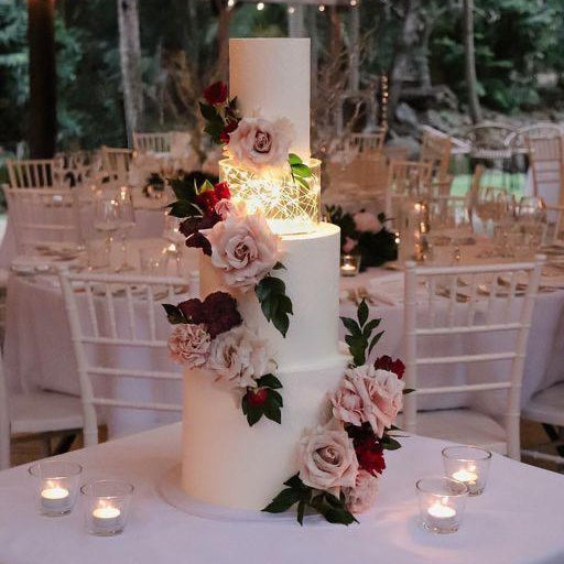 Three-tiered wedding cake with floral decorations on a table with candles, set against a blurred indoor background.