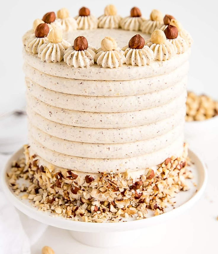 A white Belgstrew Vanilla Cake decorated with golden hazelnut praline bits and smooth cream swirls.