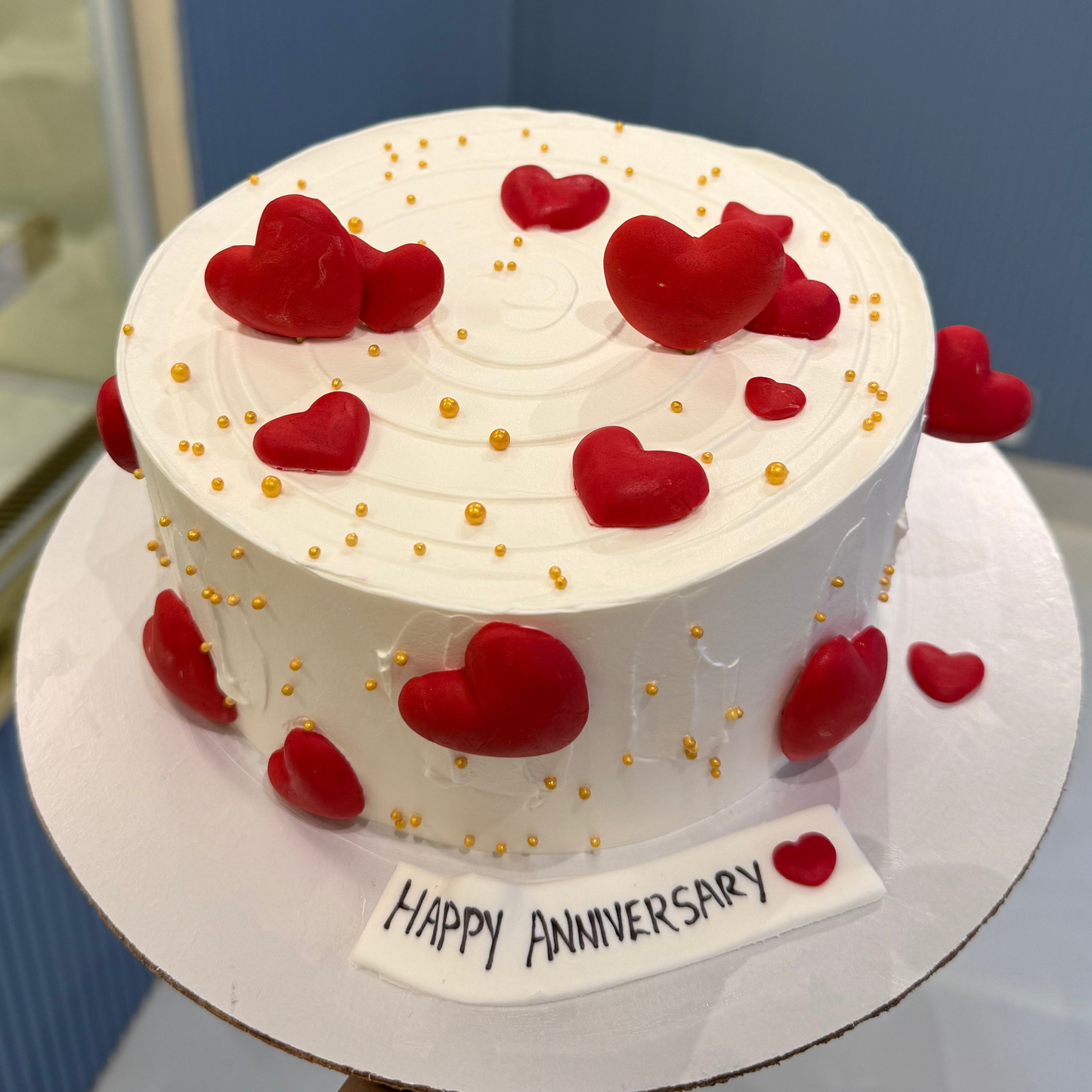 A bespoke Belgstrew Love Themed cake with red fondant hearts and elegant gold-leaf detailing on a smooth white base.
