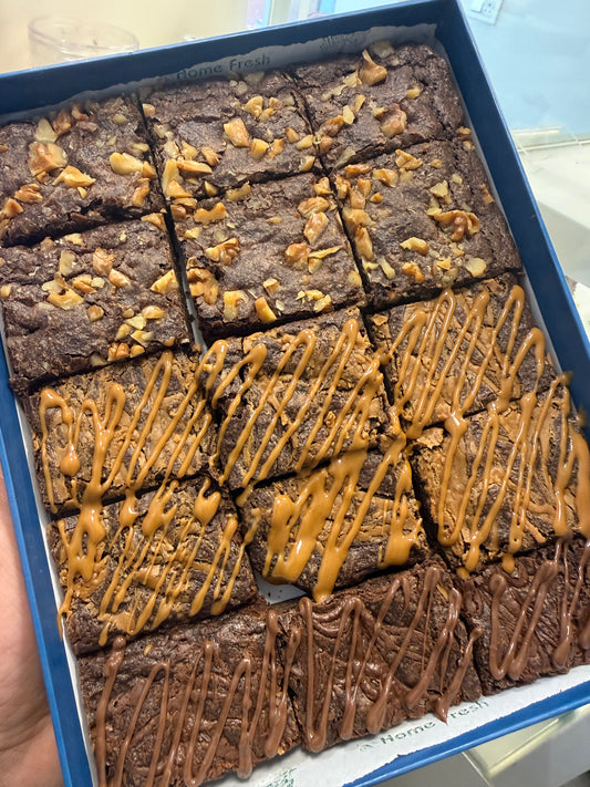 Box of brownies with different toppings including nuts and caramel drizzle.