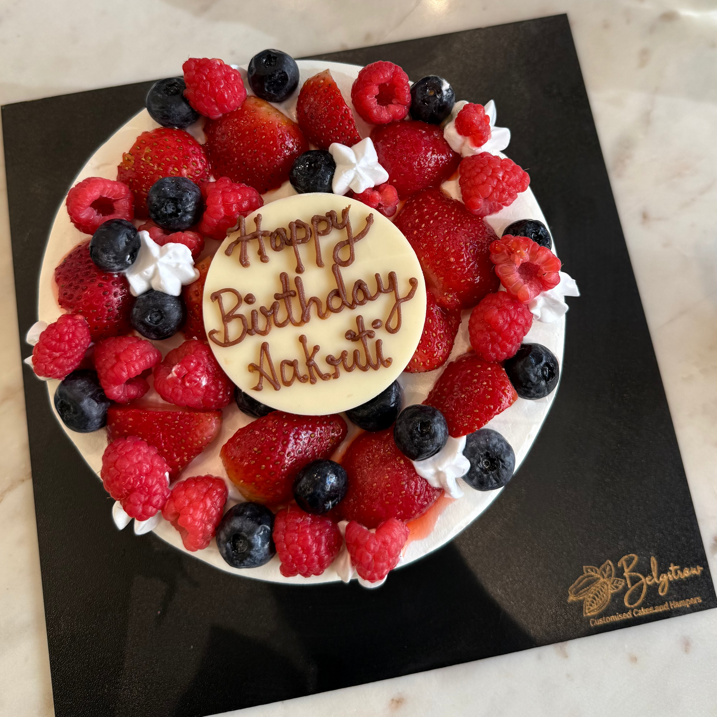 A decadent Belgstrew Chocolate Truffle Cake overflowing with fresh red strawberries, dark blueberries, and vibrant raspberries.