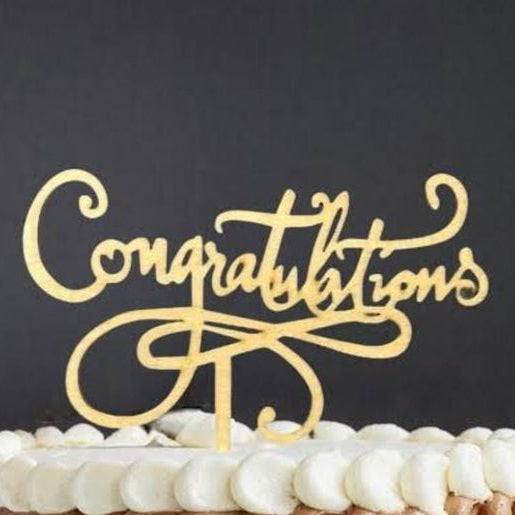 Gold 'Congratulations' cake topper on a cake with a dark background