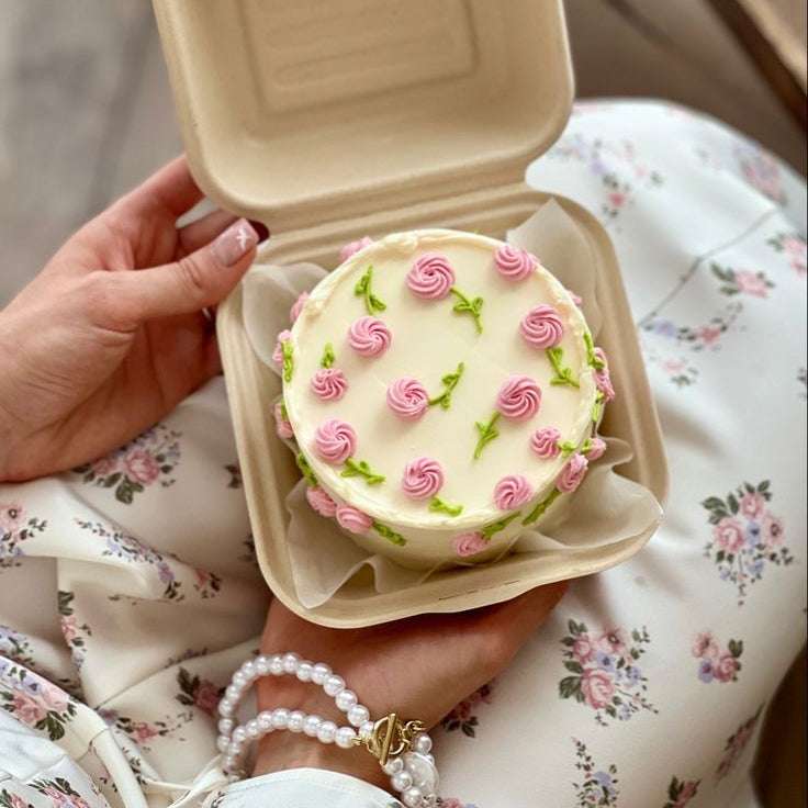 Ivory bento cake covered in small pink piped rosettes and green leaves, held in a bento box.