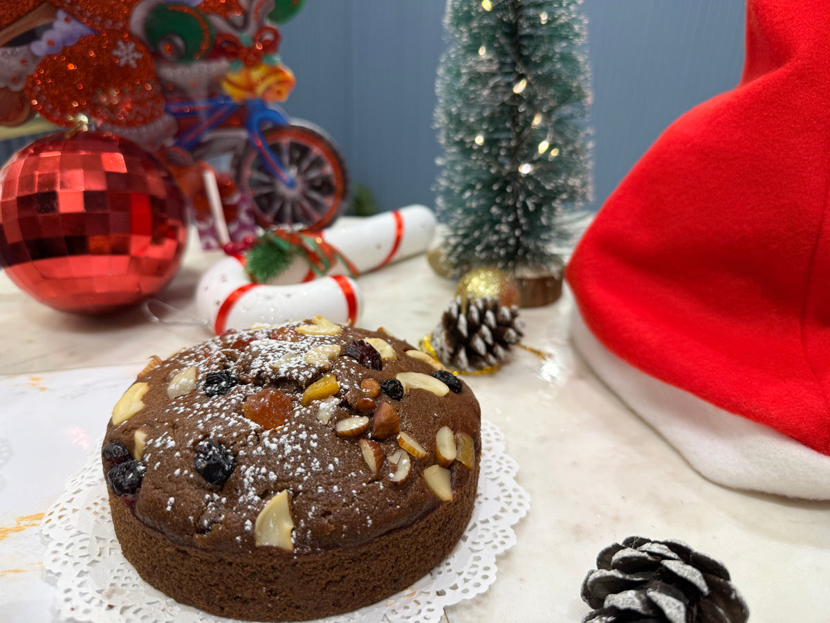 Plum cake with nuts and dried fruits on a doily, surrounded by Christmas decorations.