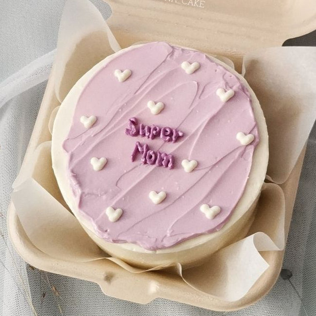 Two-tone bento cake with a textured lilac top, white heart accents, and "Super Mom" written in purple cream.