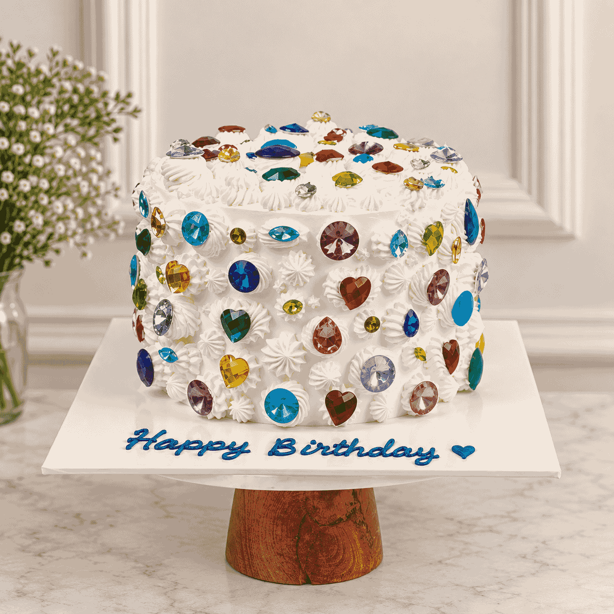 A tall ivory round celebration cake covered in piped buttercream rosettes, encrusted with colorful faceted crystal gems, with blue Happy Birthday script on the board.