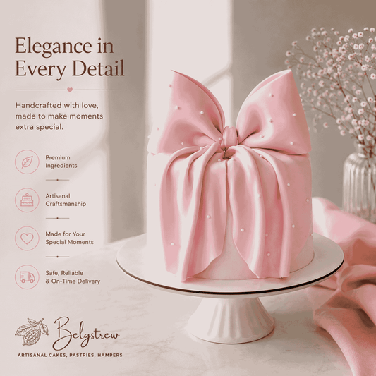 A round ivory celebration cake topped with an oversized sculpted matte blush pink bow draped over the sides and dotted with delicate white sugar pearls.