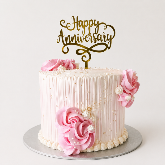 A tall light pink anniversary cake with vertical combed texture lines, decorated with large piped pink rosettes, white pearls, and a gold Happy Anniversary script topper.