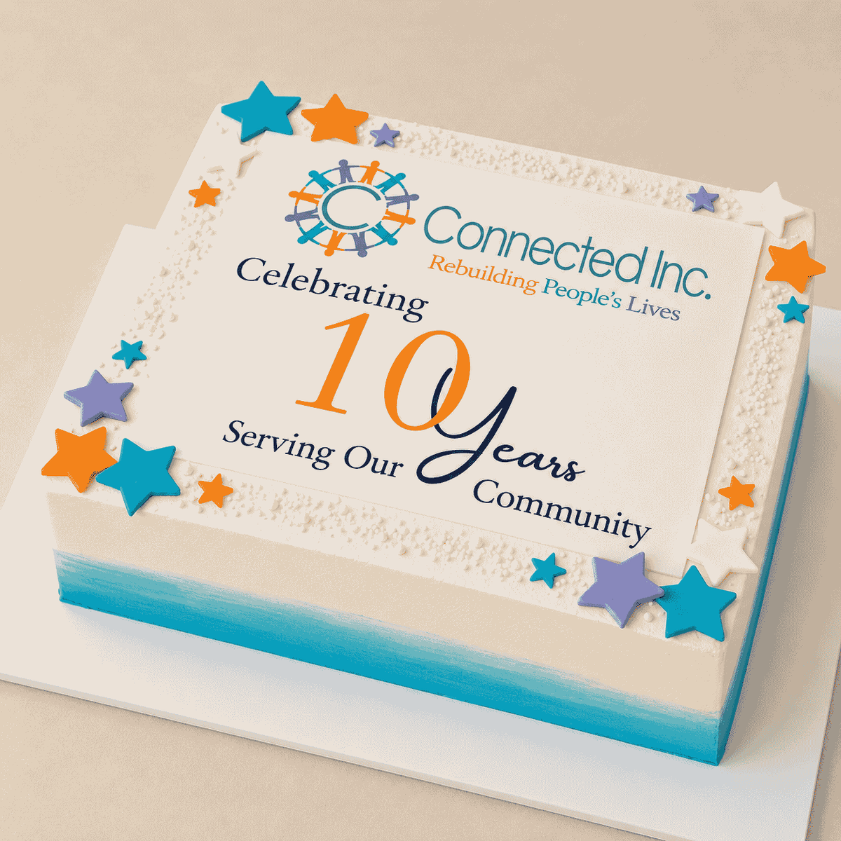 A large rectangular white corporate anniversary sheet cake with a teal bottom border, featuring a central edible print reading Connected Inc. Celebrating 10 years Serving Our Community, framed by small white sugar pearls and colorful fondant stars.
