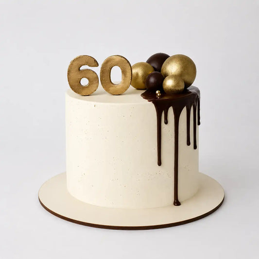 A tall round 60th birthday cake for him with a smooth white cream base, featuring a dark chocolate drip down the side, topped with large gold and brown spheres and a gold number 60.