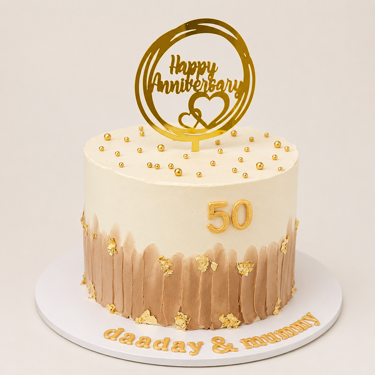 A premium round 50th anniversary cake with a smooth white top and a textured light brown brushstroke bottom, decorated with gold leaf flakes, gold pearls, and a gold number 50.
