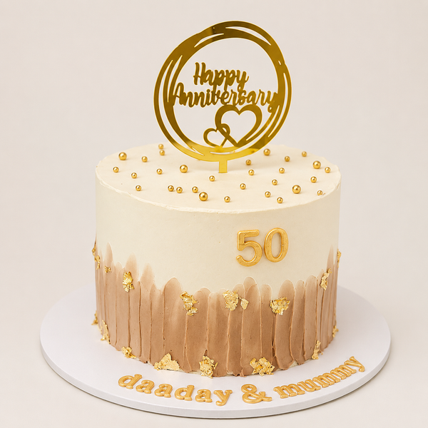 A premium round 50th anniversary cake with a smooth white top and a textured light brown brushstroke bottom, decorated with gold leaf flakes, gold pearls, and a gold number 50.