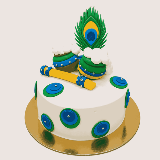 A round white festive cake decorated with layered peacock feather medallions, topped with two butter pots spilling white cream, a yellow flute, and a peacock feather.