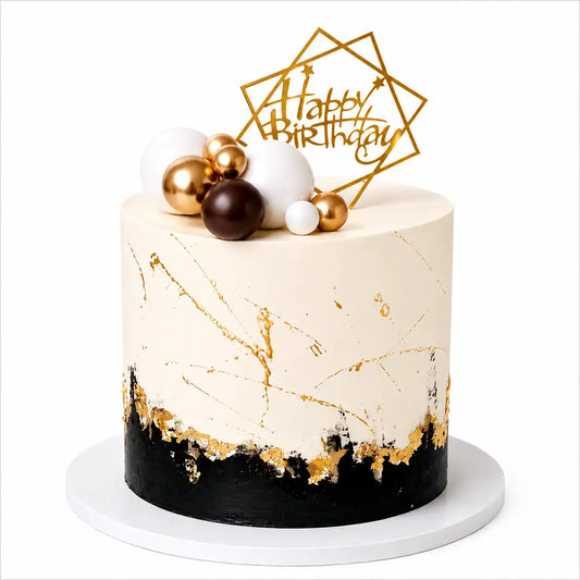 A tall round premium birthday cake for him with a smooth white cream top half with gold splatters, a jagged black bottom layer lined with gold leaf, topped with white, gold, and brown spheres and a geometric gold topper as seen in image.