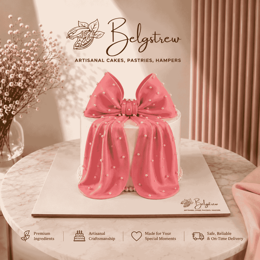 A tall round white frosted cake decorated with a large handcrafted pink bow studded with white sugar pearls draping down the front.