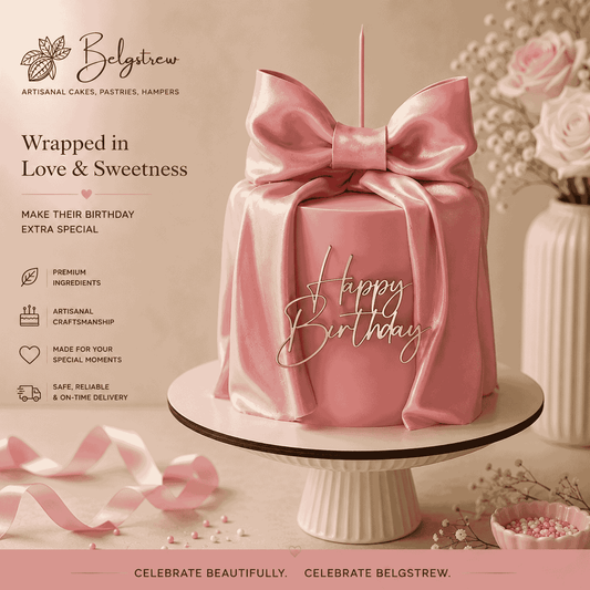A tall round pastel pink celebration cake on a fluted stand, wrapped in a large sculpted pink bow with pearlescent sheen and a gold Happy Birthday topper.