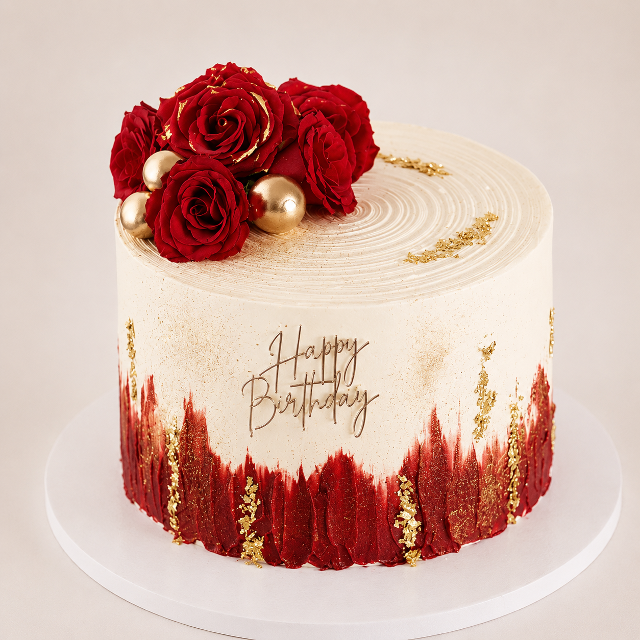 A tall ivory birthday cake with textured top swirls and a bold red brushstroke bottom half, decorated with edible gold leaf, gold spheres, and a cluster of fresh red roses.