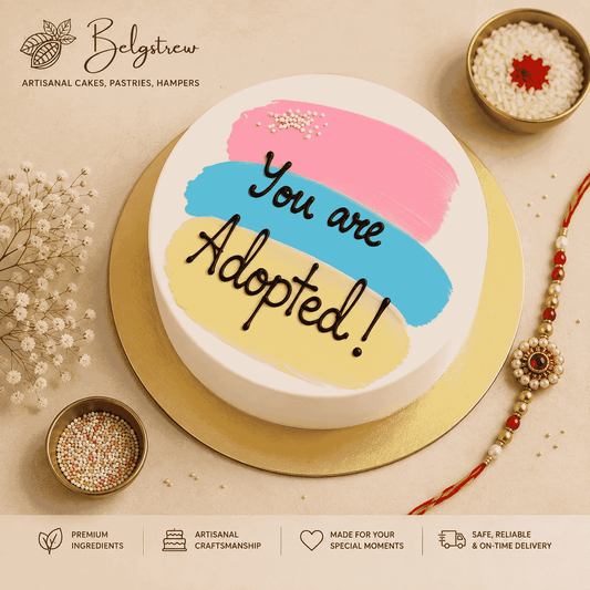 A round white frosted festive cake with pastel pink, blue, and yellow painted brushstrokes and black cursive script reading You are Adopted.