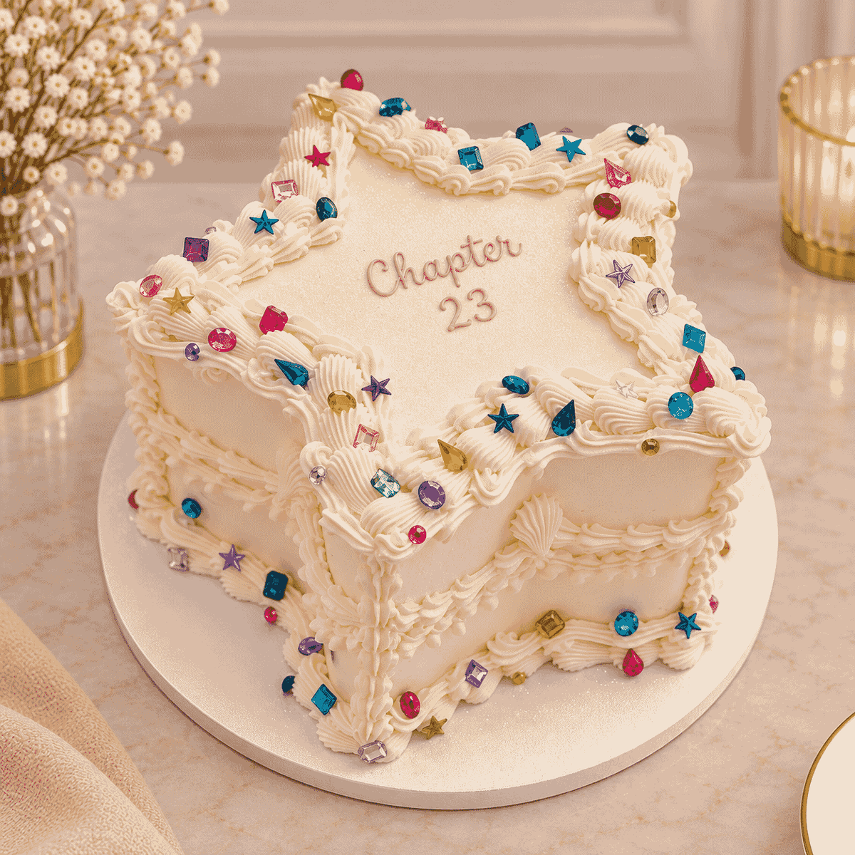 A five-pointed star shaped ivory vintage Lambeth cake decorated with piped shell borders, colorful faceted gemstone crystals, and Chapter 23 script.