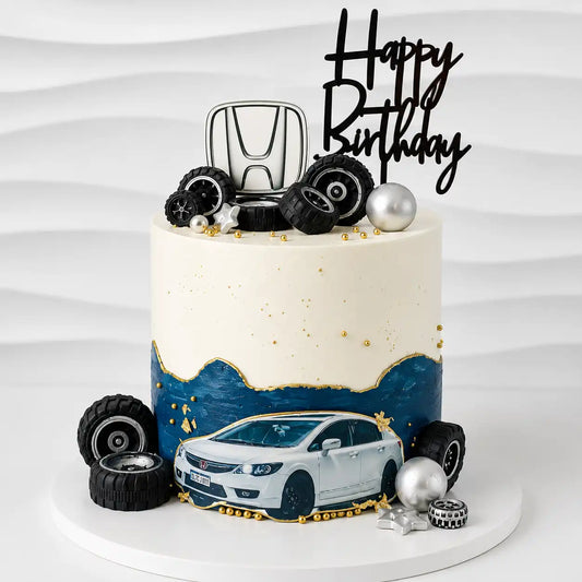 A tall round premium birthday cake featuring a smooth white top half and a blue fault line bottom half decorated with gold trim, realistic black toy tires, a white sedan graphic cutout, and a silver Honda brand logo on top as seen in image.